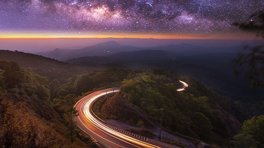 Time lapse photo of cars on a mountainous road at night.