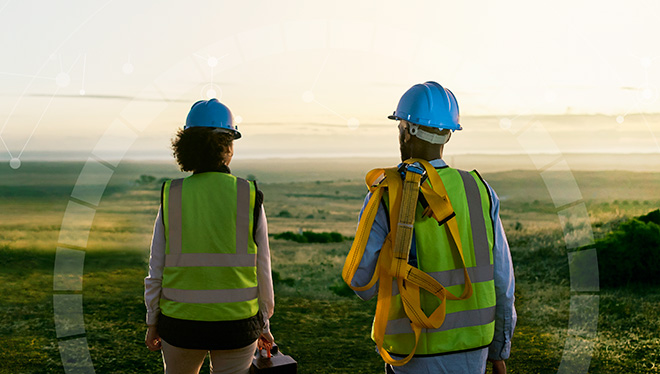 A woman and a man, both installers, standing and looking at a green landscape during sunrise.