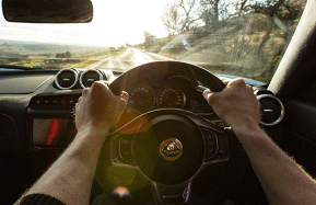 Lotus car interior and a person holding sterring wheel driving on a country road